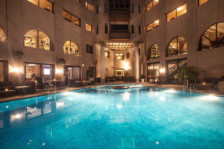 Piscine extérieure de l'Hivernage Hotel & Spa illuminée la nuit avec des palmiers et des lumières